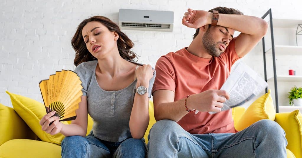 Man and woman fanning themselves because AC is running but hot inside Ocala home