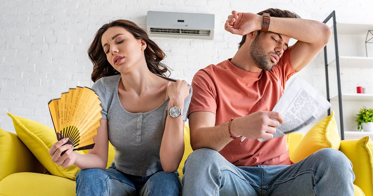 Man and woman fanning themselves because AC is running but hot inside Ocala home